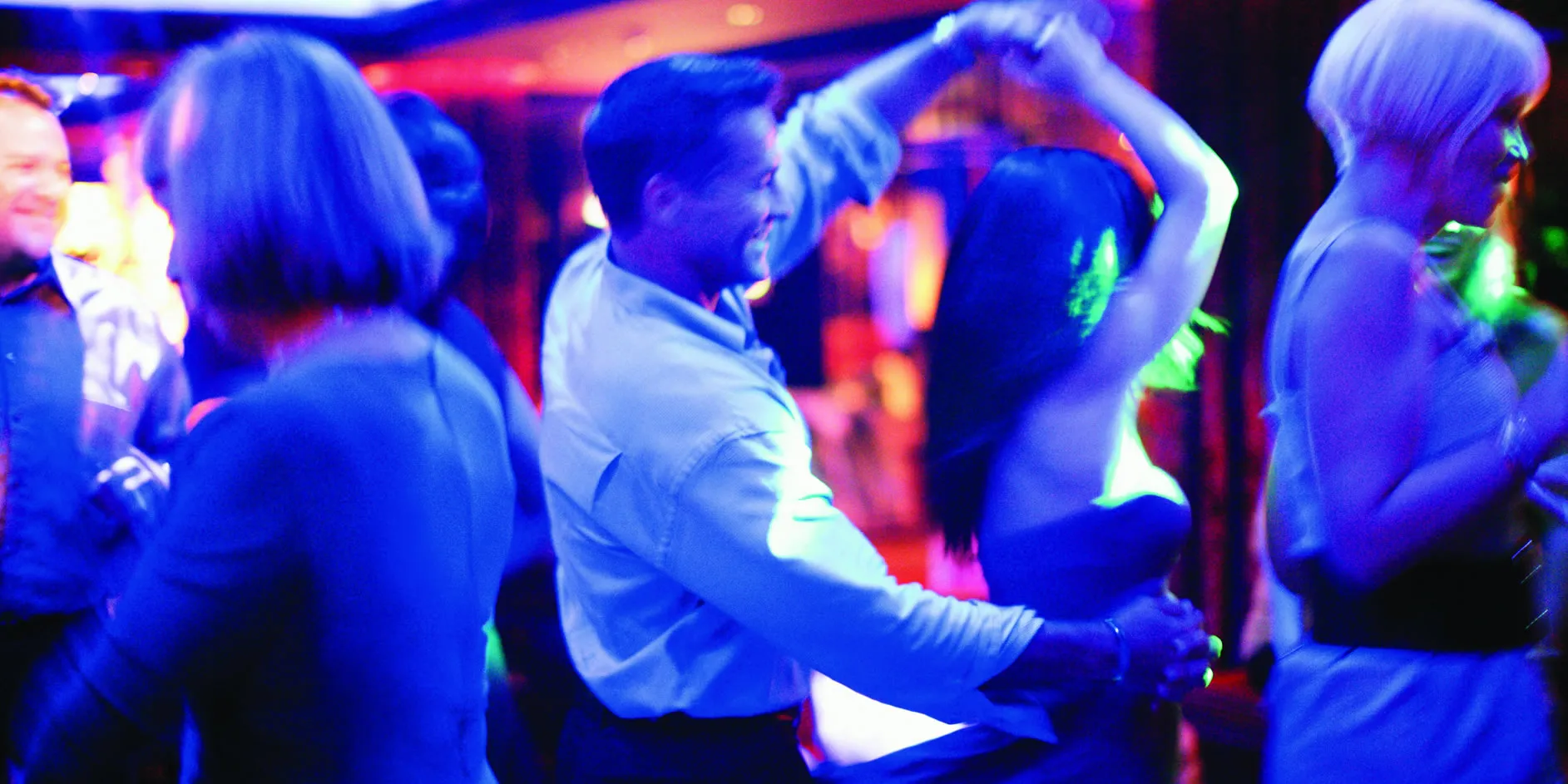 People dancing together in a vibrant nightclub with colorful blue lighting