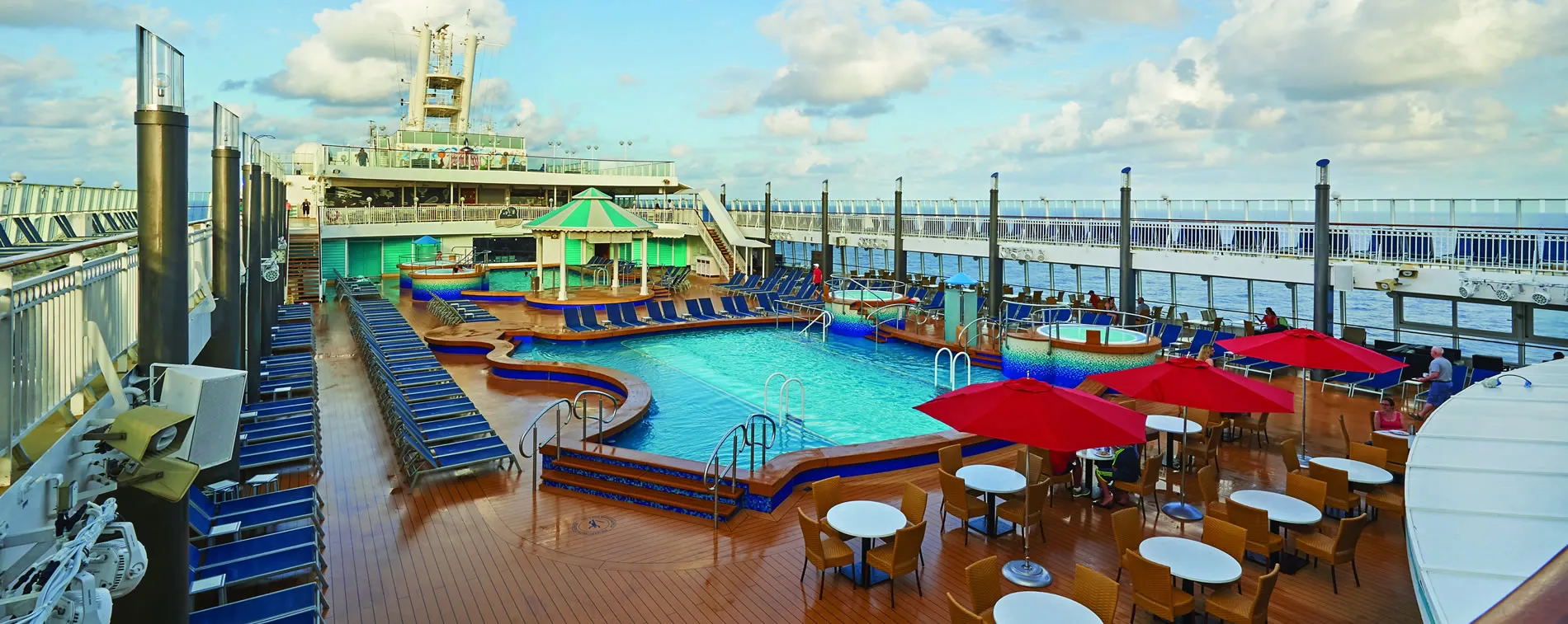 Cruise ship deck with swimming pool, lounge chairs, and red umbrellas