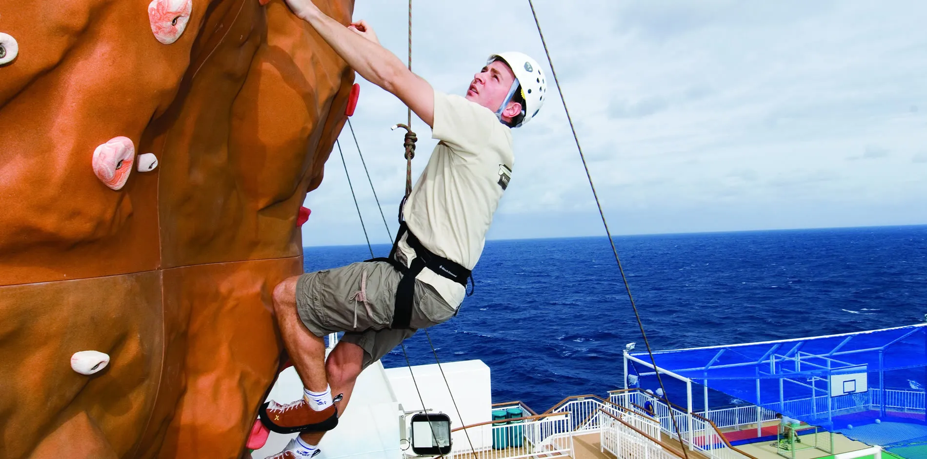 Rock climber scaling wall on cruise ship deck with ocean backdrop