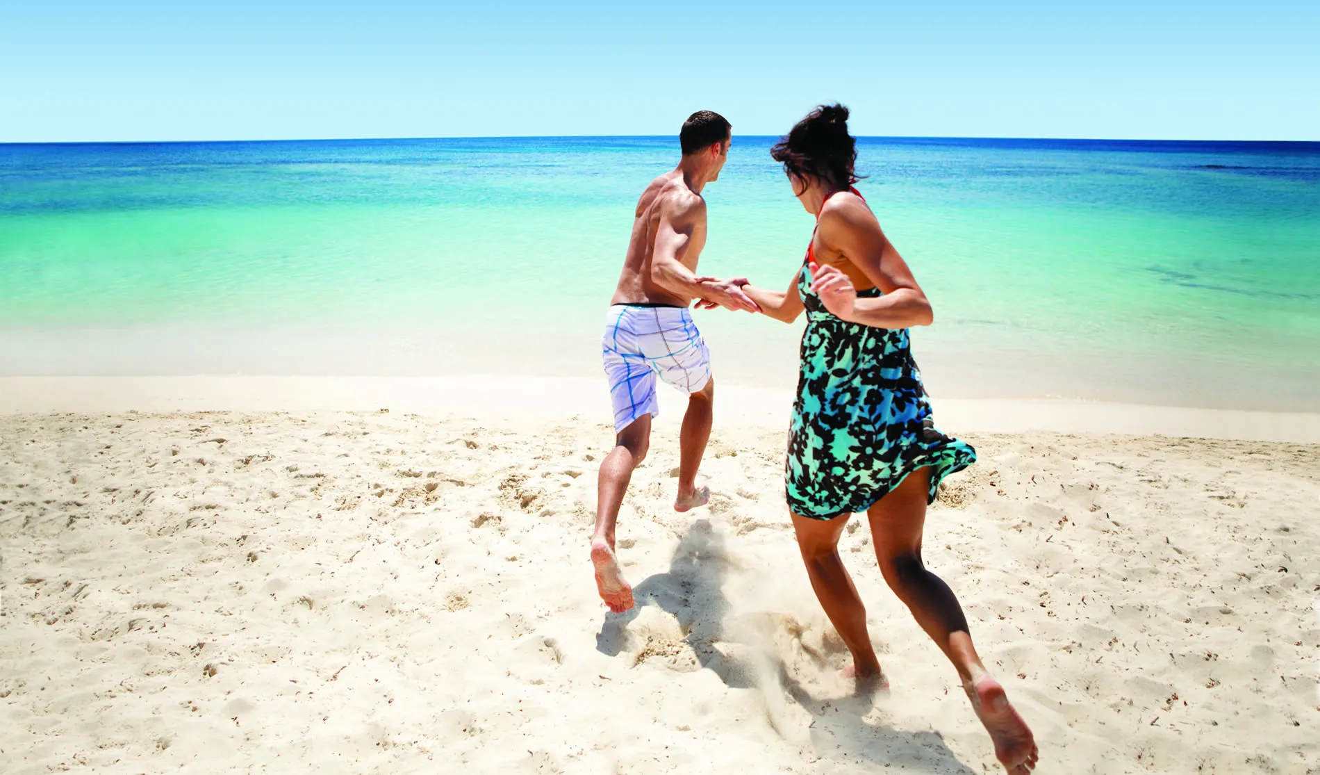 Two people running and holding hands on a tropical turquoise beach