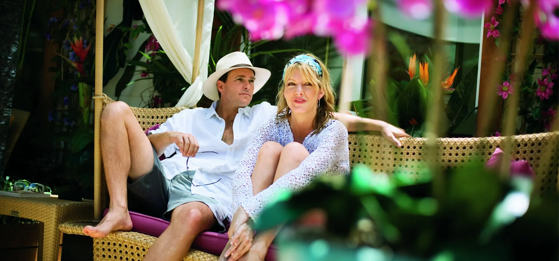 Couple relaxing on woven chairs surrounded by tropical flowers and plants