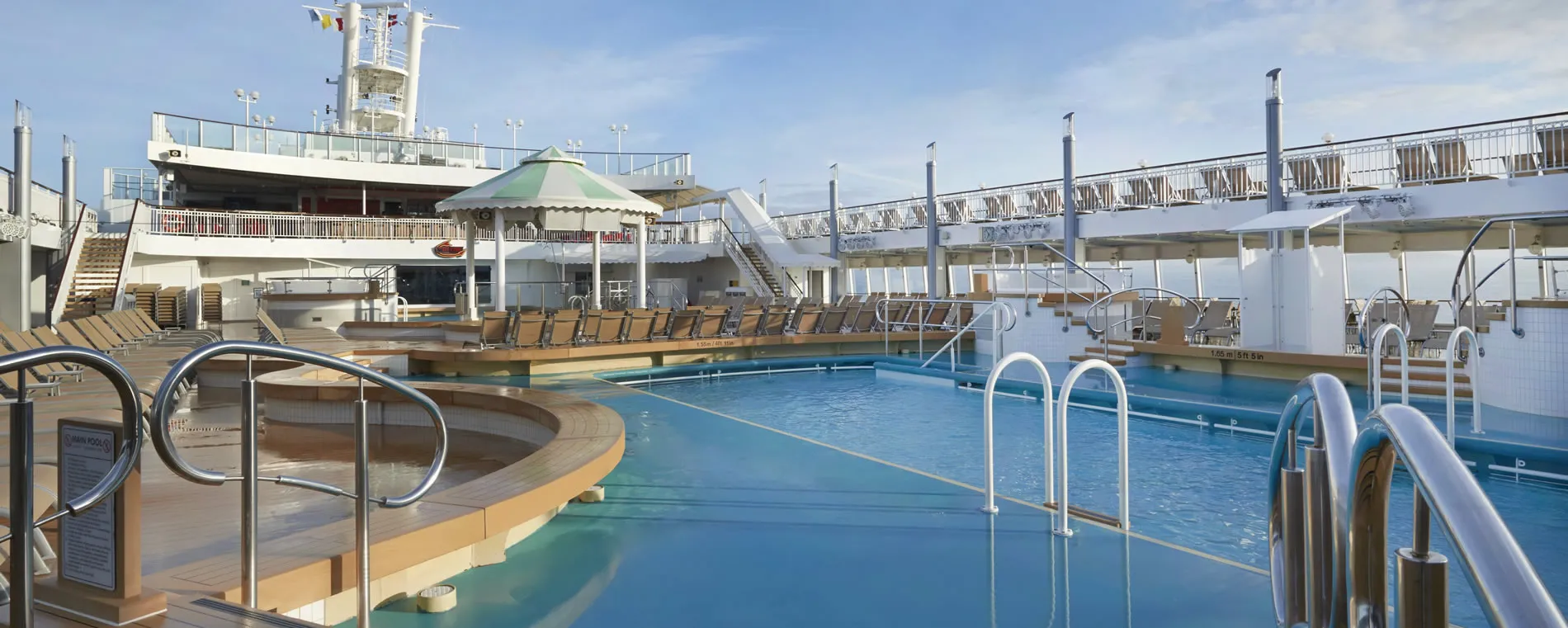 Cruise ship pool deck with blue water, lounge chairs, and sunny sky