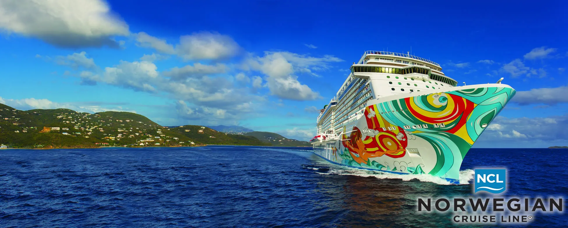 Colorful Norwegian Cruise Line ship sailing near tropical mountainous coastline