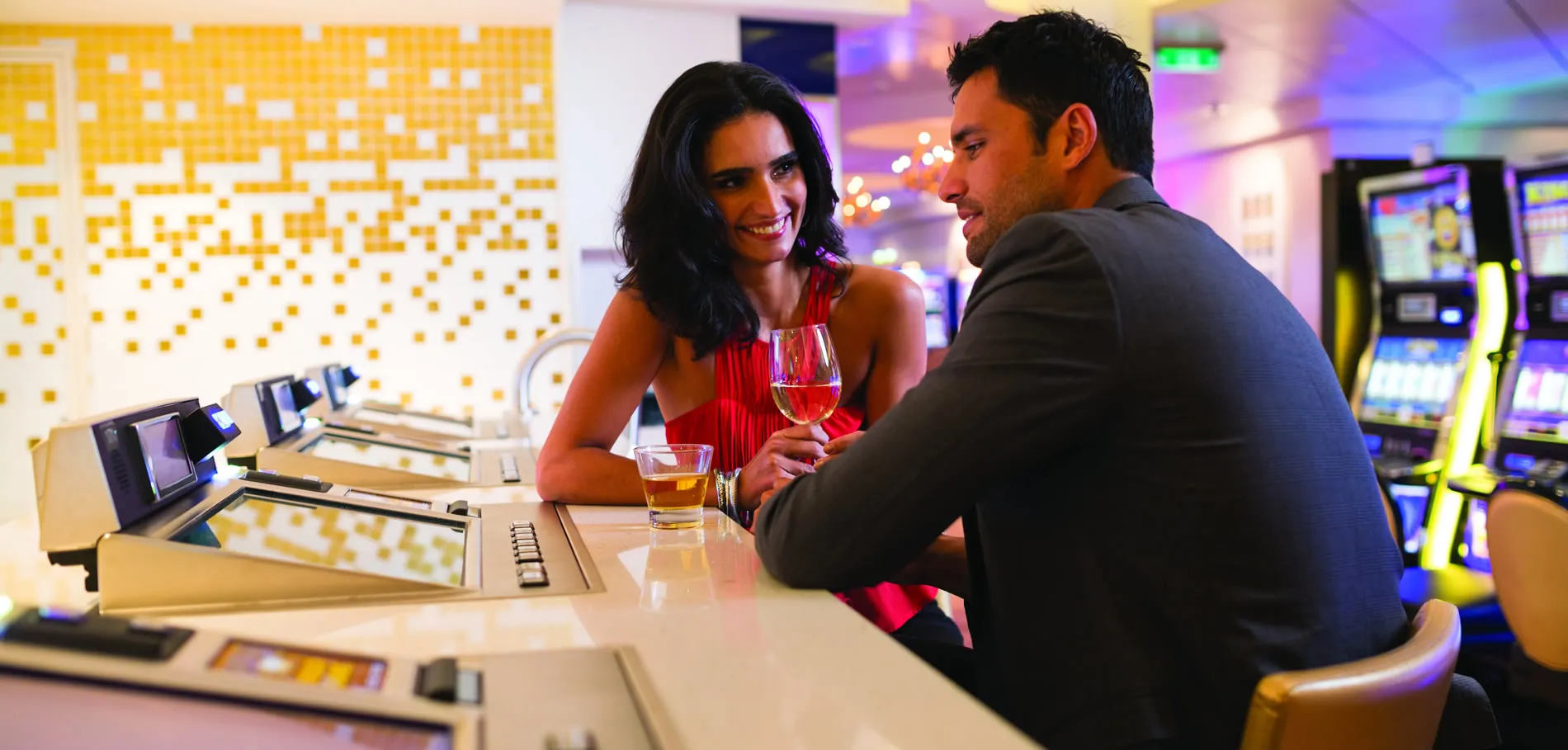 Couple enjoying drinks at a casino gaming table with slot machines
