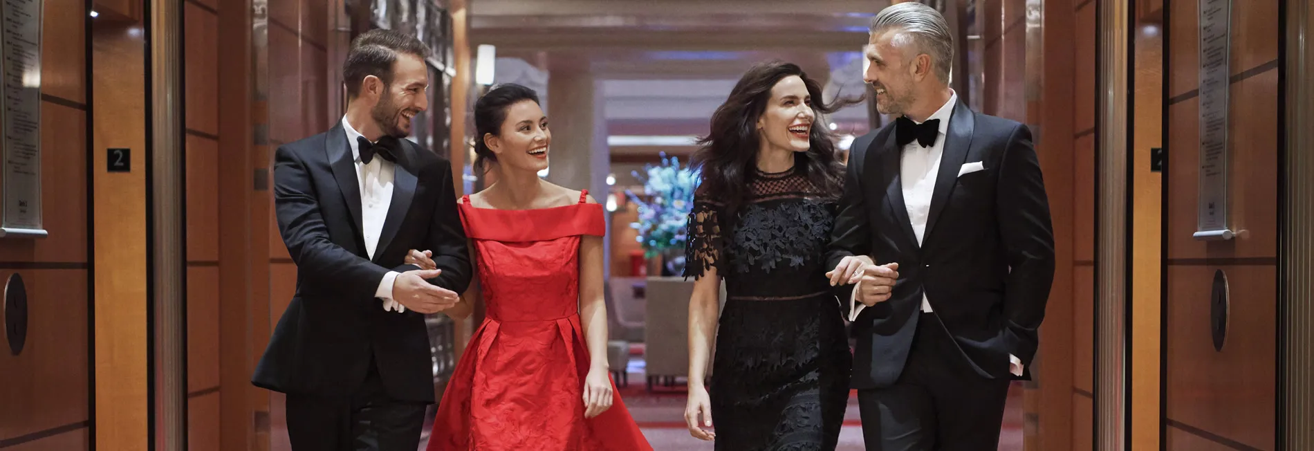 Two couples dressed formally, smiling and walking together in elegant hallway