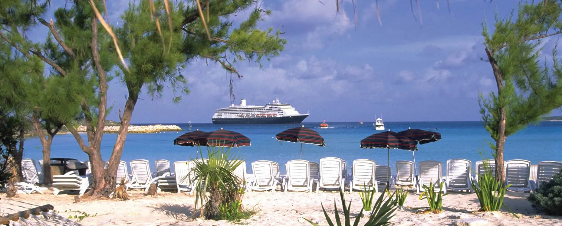 Tropical beach with white chairs, umbrellas, and cruise ship in background