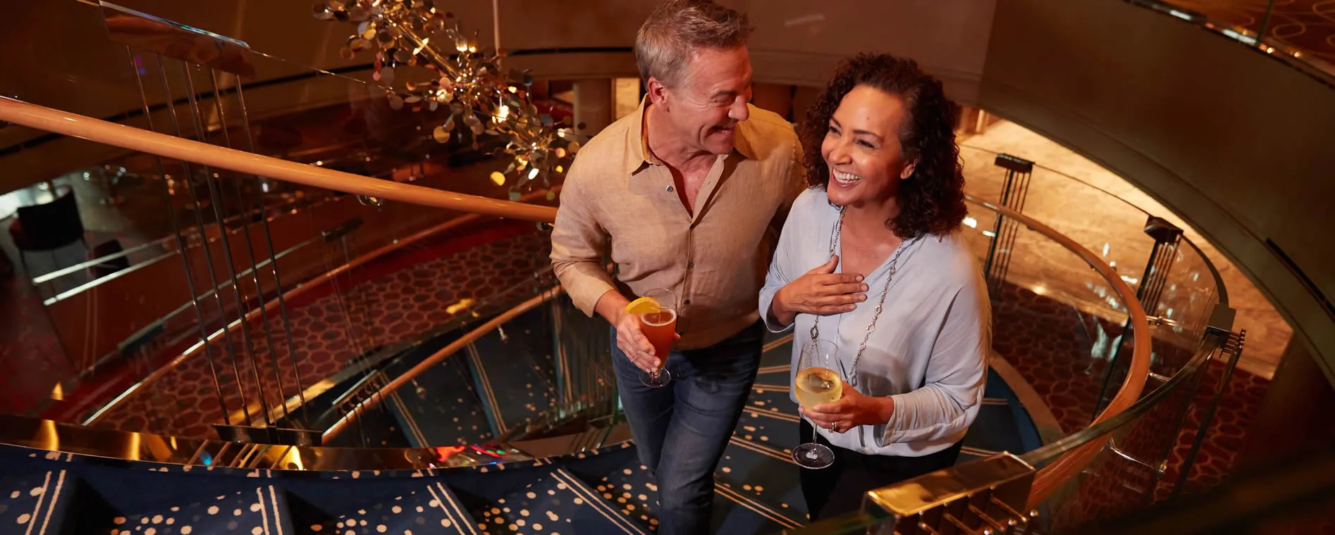 Couple laughing together on elegant spiral staircase with drinks