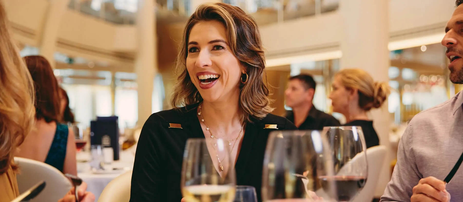 Smiling woman in black jacket enjoying conversation at restaurant with wine glasses