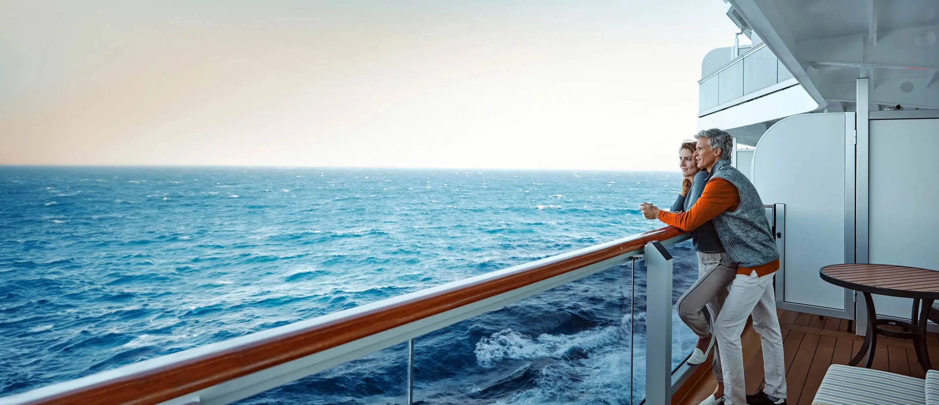 Two people on cruise ship balcony looking out at vast blue ocean