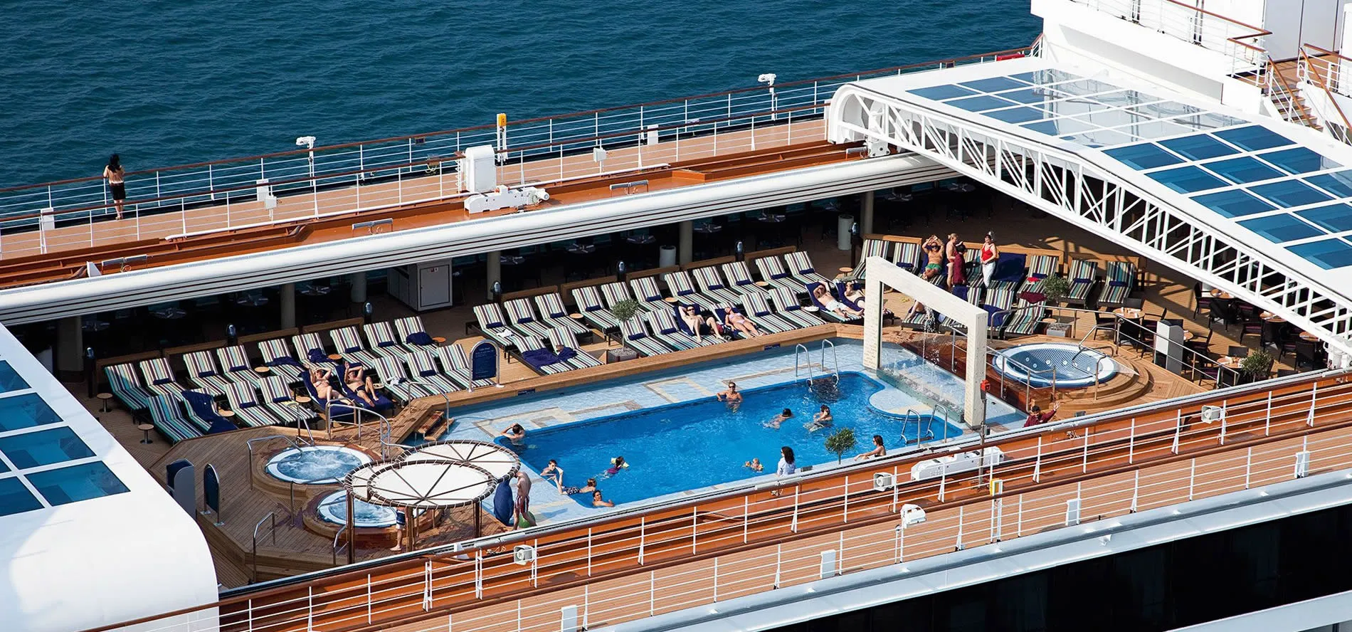 Cruise ship deck with swimming pool, hot tubs, and lounge chairs by ocean