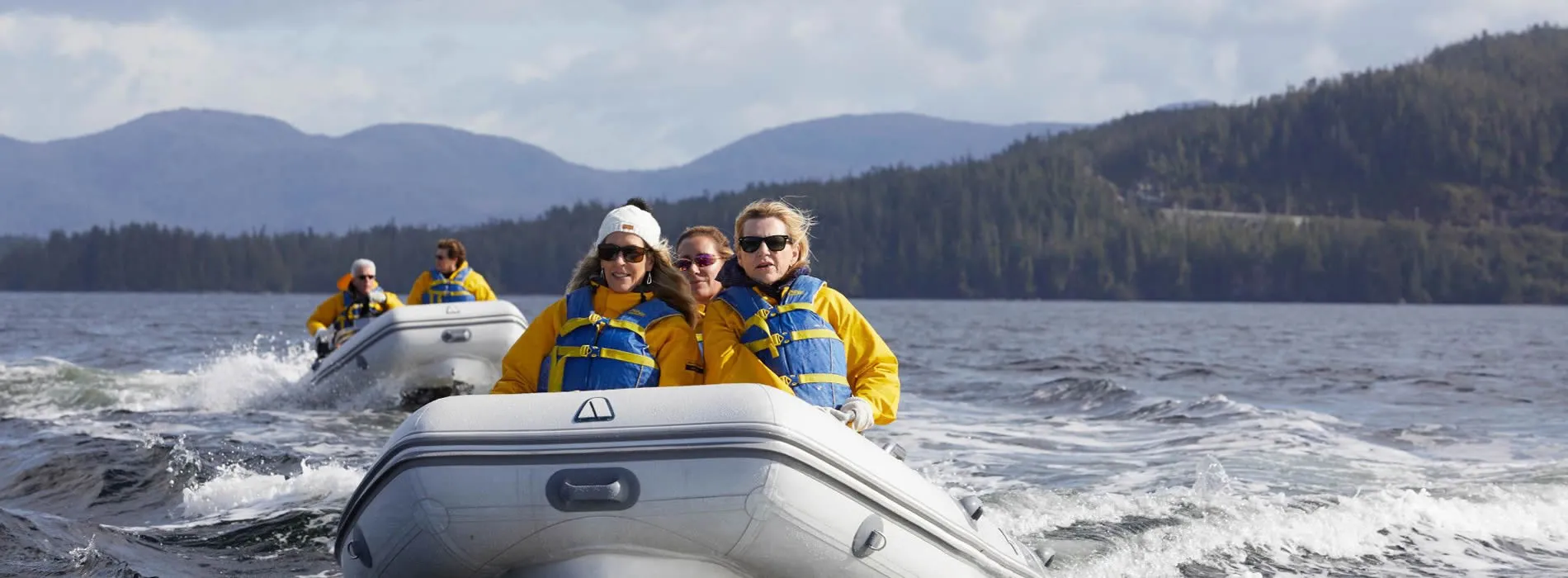 People in yellow jackets riding inflatable boats on mountain lake