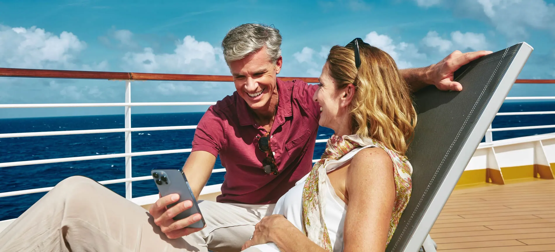 Couple laughing on cruise ship deck with ocean and blue sky background