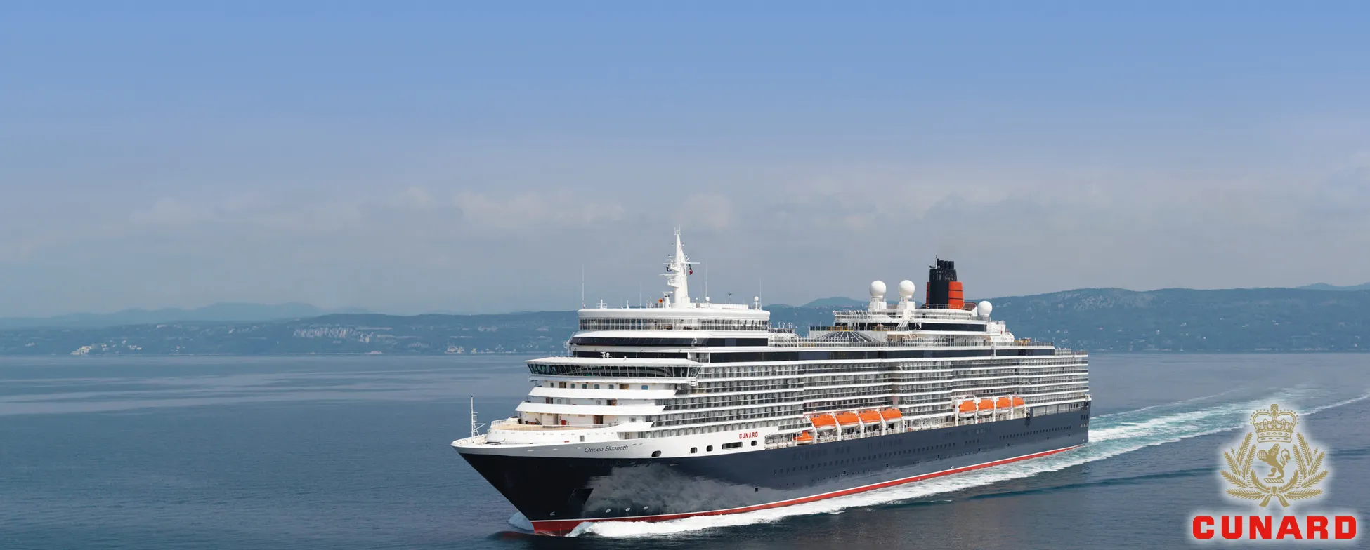 Cunard cruise ship sailing on calm blue waters with mountains in background