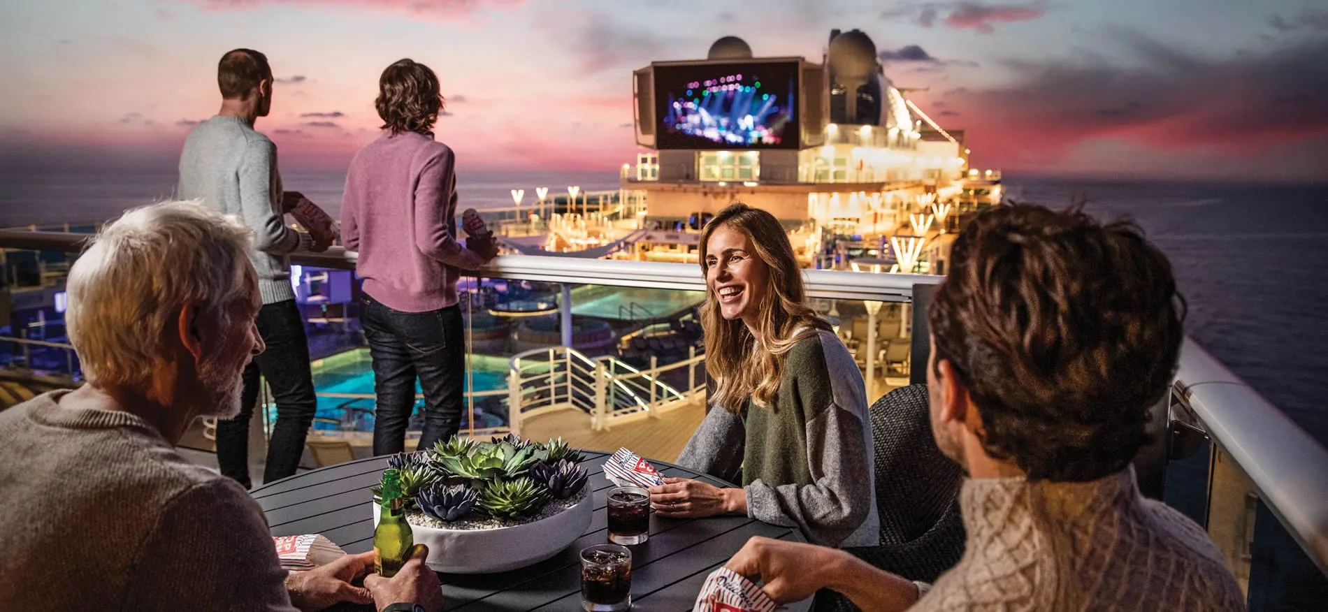 People enjoying drinks on a cruise ship deck at sunset with live music
