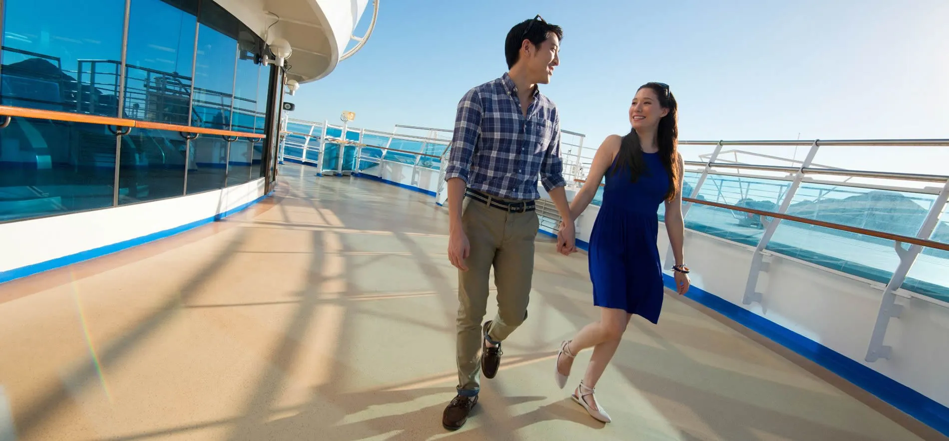 Couple walking hand in hand on a sunny cruise ship deck