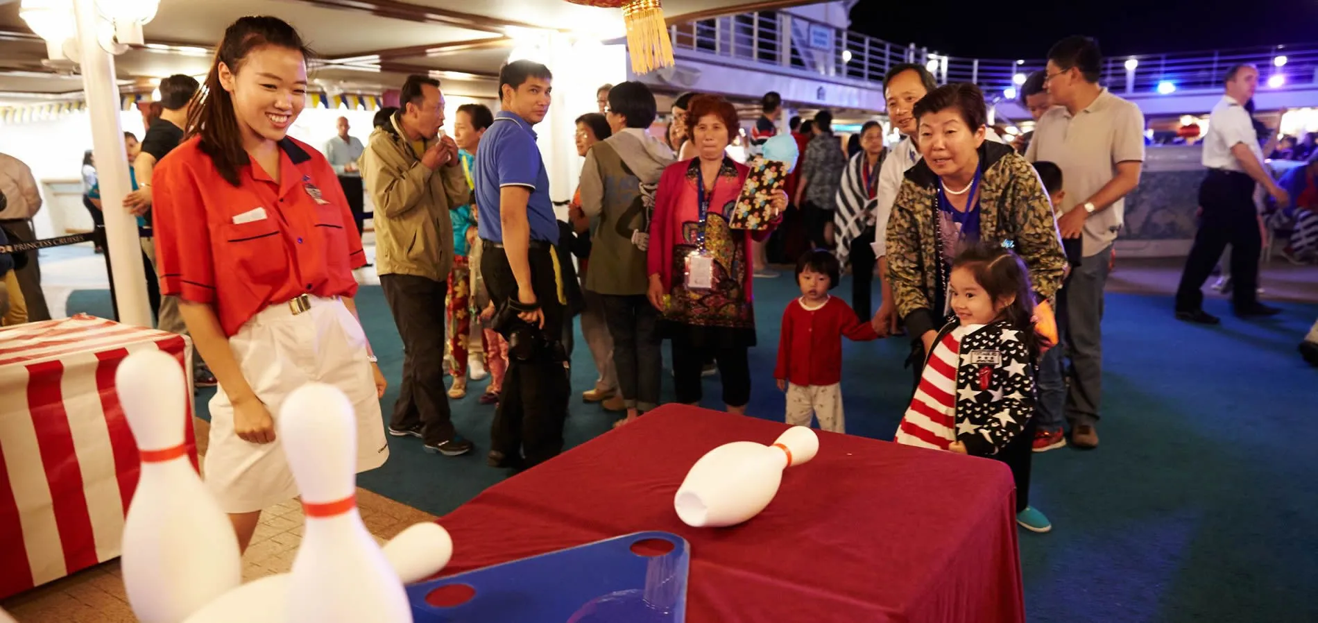 Staff member demonstrates bowling game to crowd on cruise ship deck