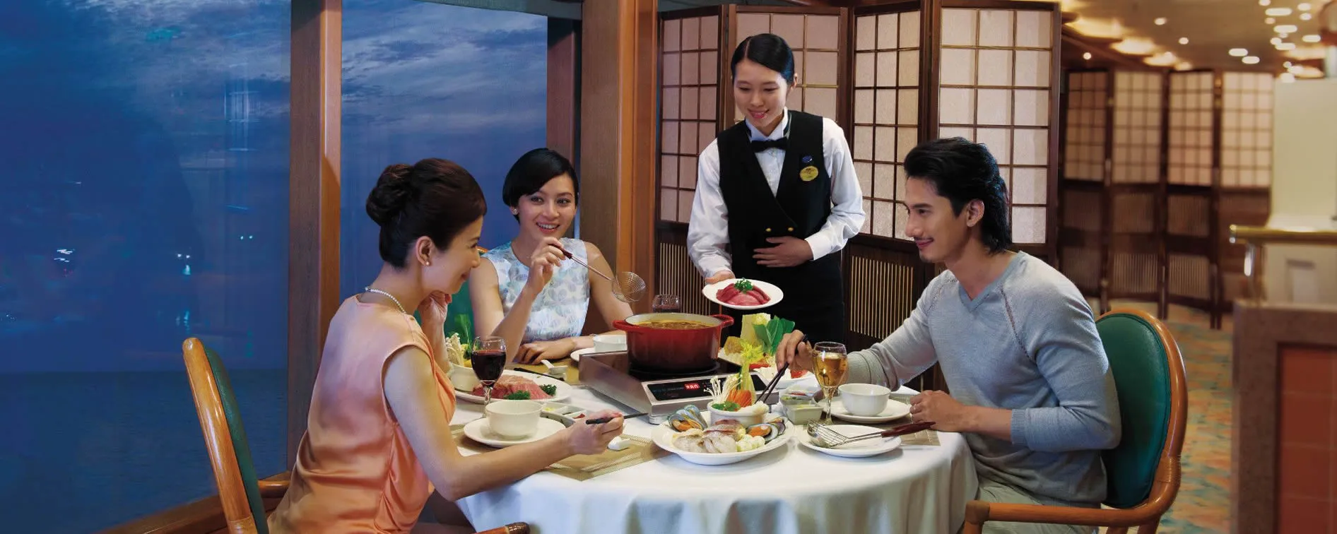 Couple dining at elegant restaurant with server, enjoying hot pot and drinks