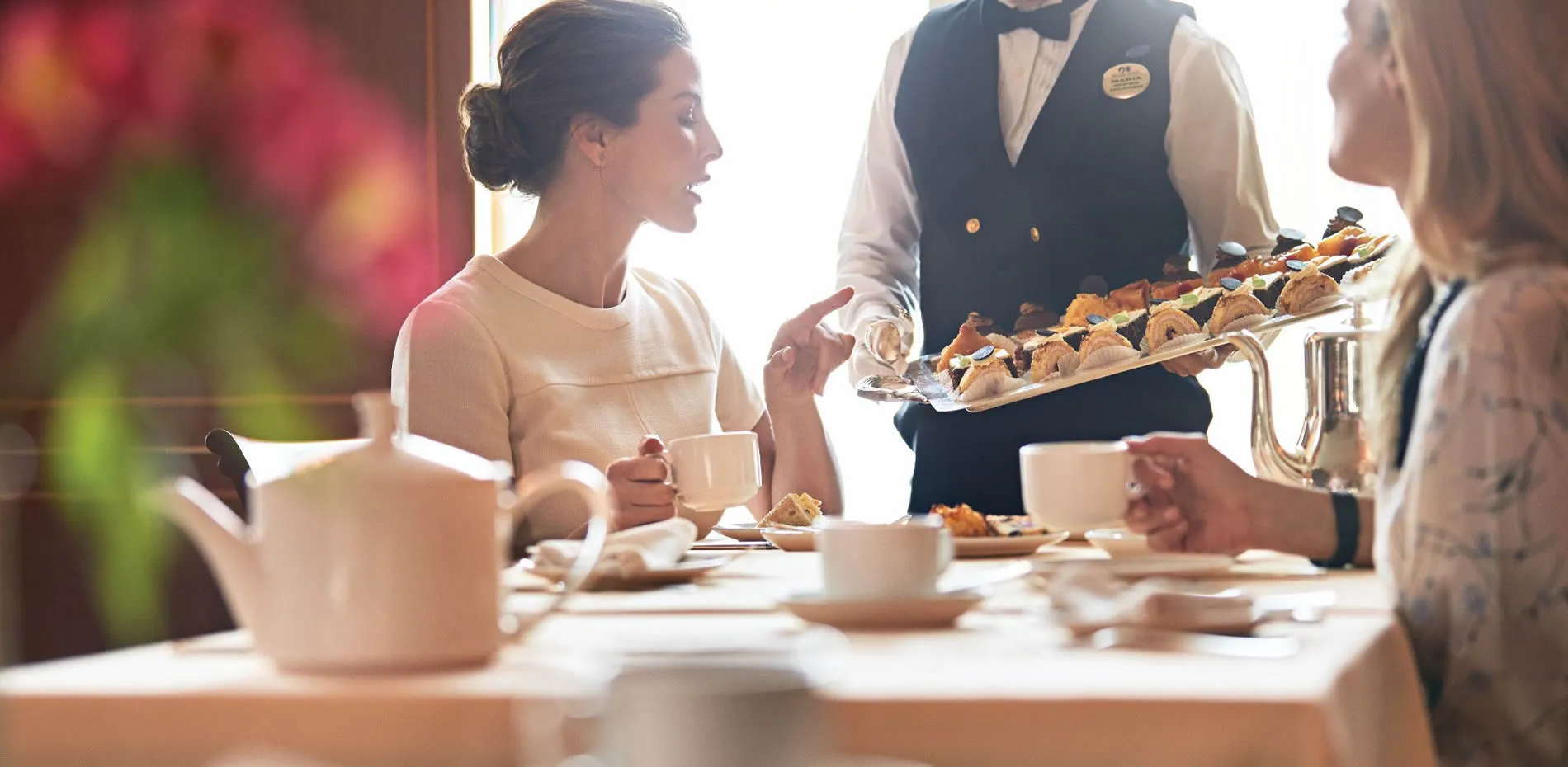 Elegant afternoon tea service with waiter serving pastries to guests