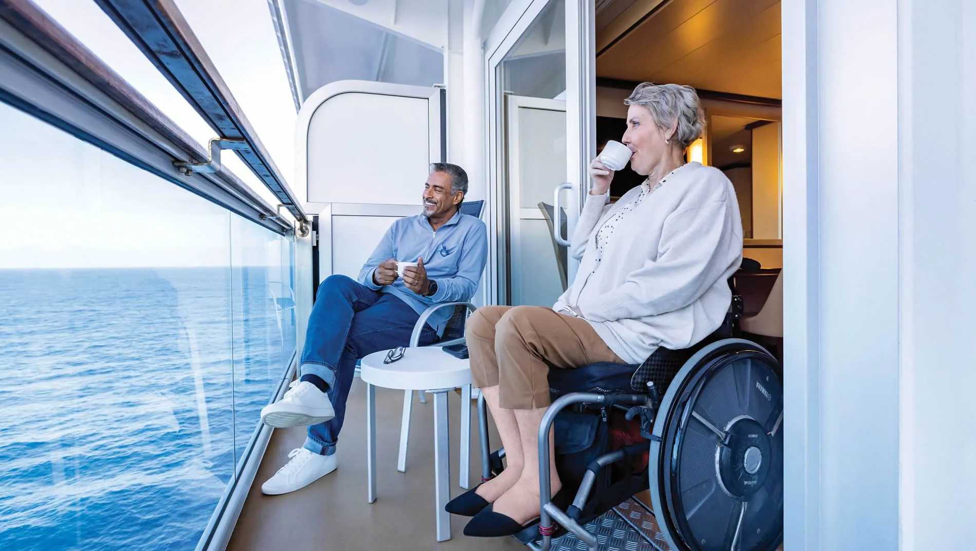 Two people enjoying coffee on a cruise ship balcony with ocean view