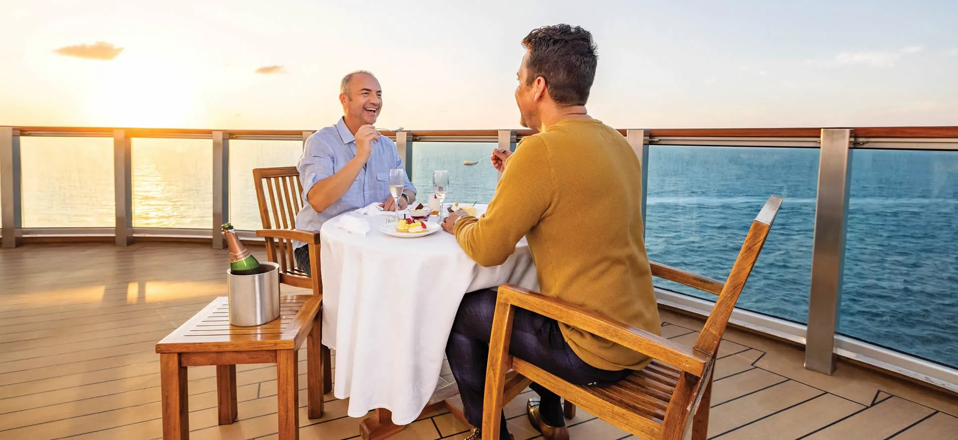 Two men enjoying a meal on a cruise ship deck at sunset