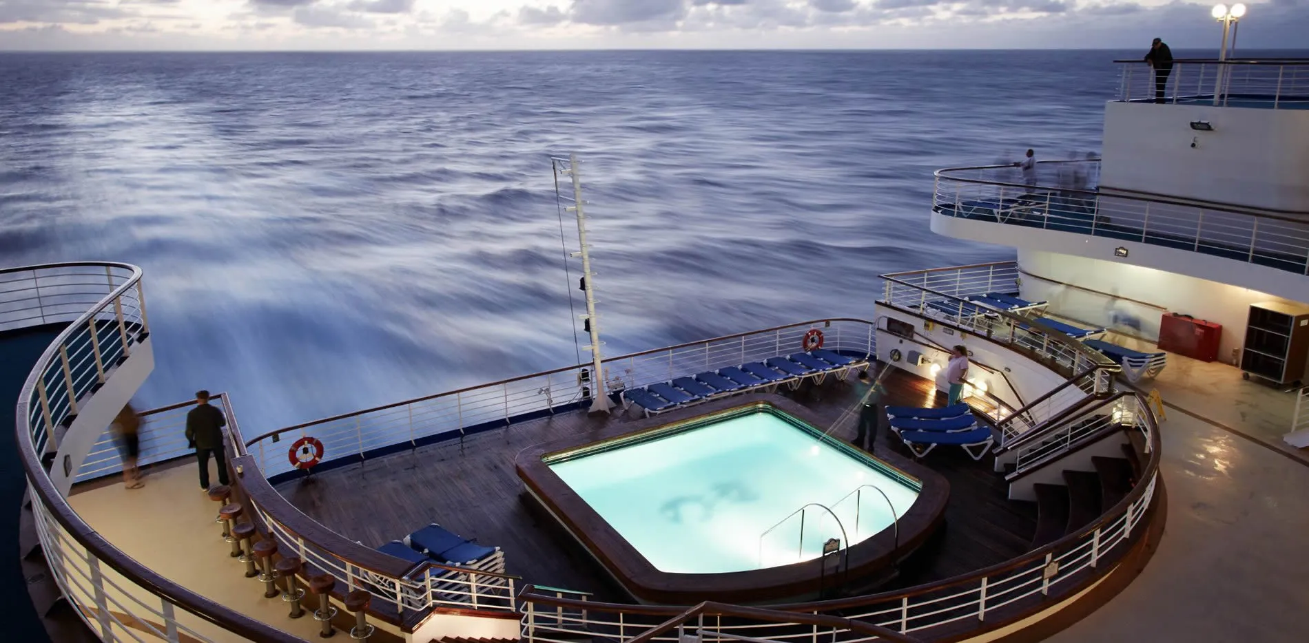 Cruise ship deck with illuminated pool overlooking calm ocean at dusk