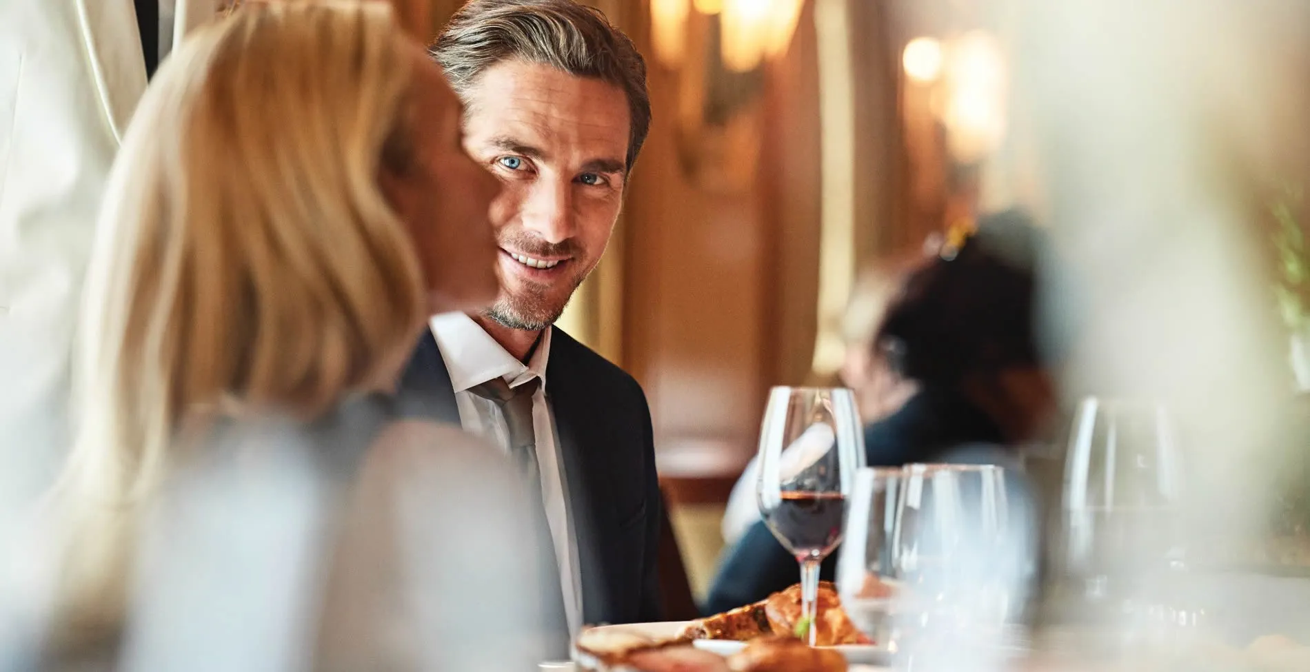 Smiling well-dressed man enjoying dinner with companion at restaurant