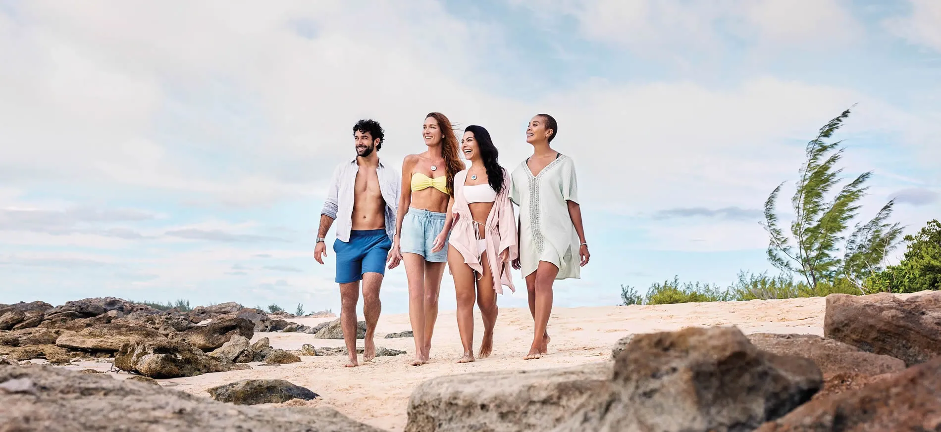 Four friends walking together on rocky beach under cloudy sky