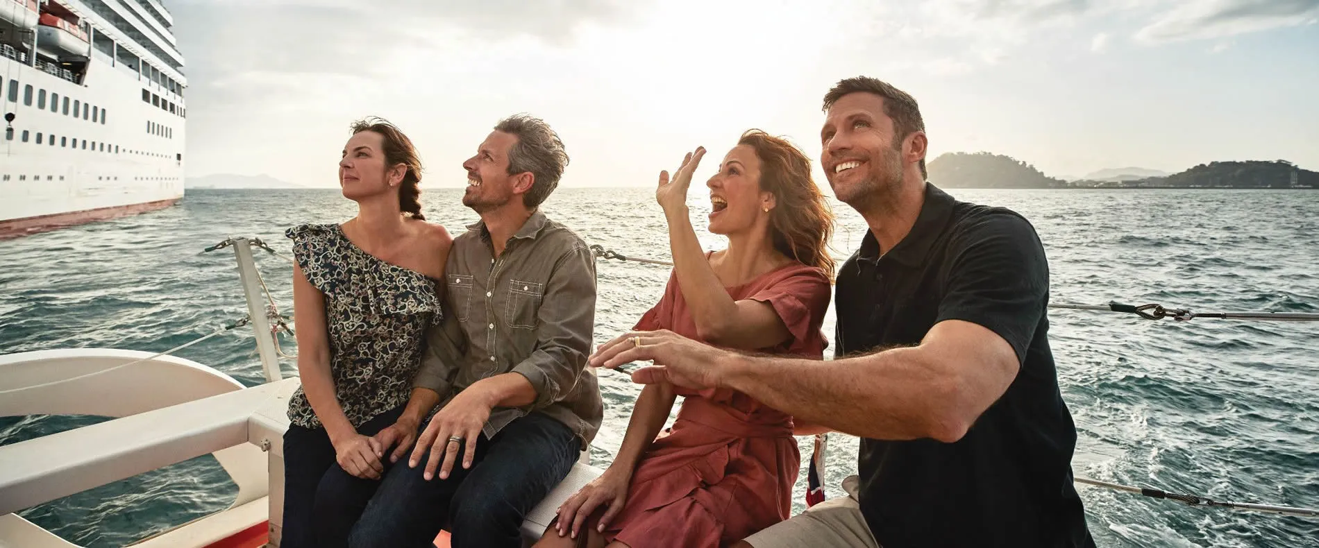 Four friends enjoying a sunny cruise, laughing with cruise ship behind them