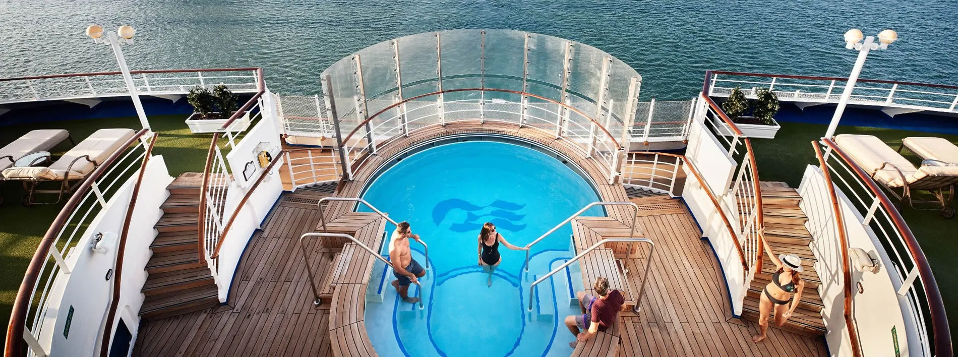 Cruise ship deck with blue pool, wooden deck, and ocean view