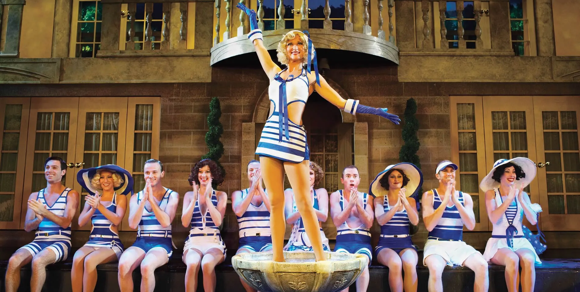 Theater performers in blue and white nautical costumes on stage