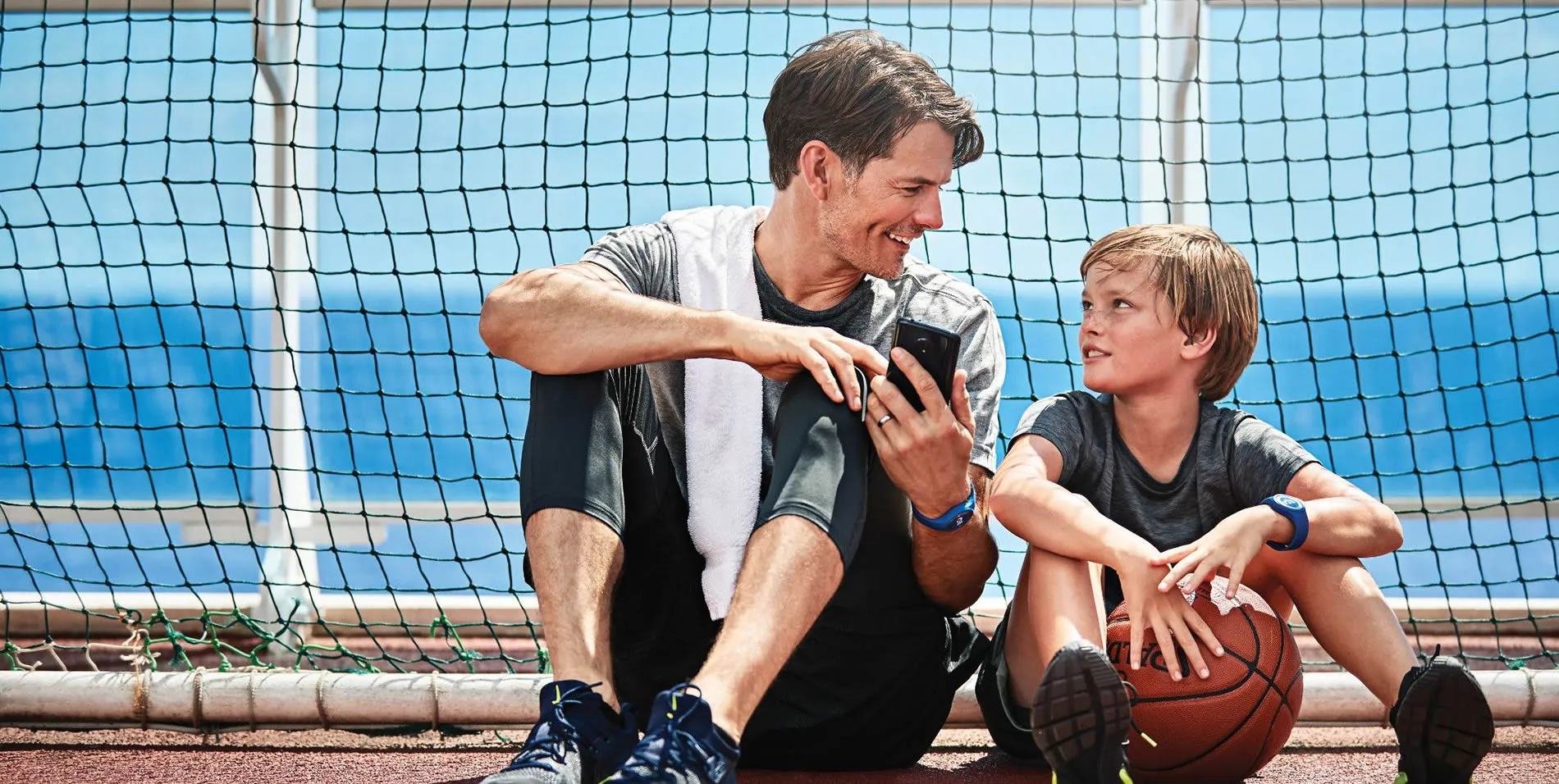 Father and son sitting together after basketball practice, looking at phone