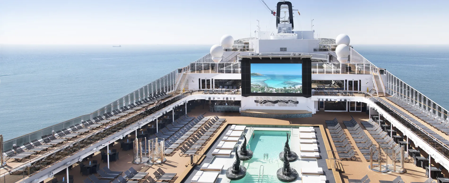 Cruise ship deck with swimming pool, lounge chairs, and large outdoor screen