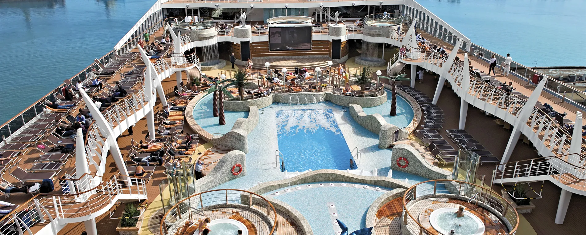 Luxurious cruise ship deck with swimming pools, hot tubs, and sunbathing areas