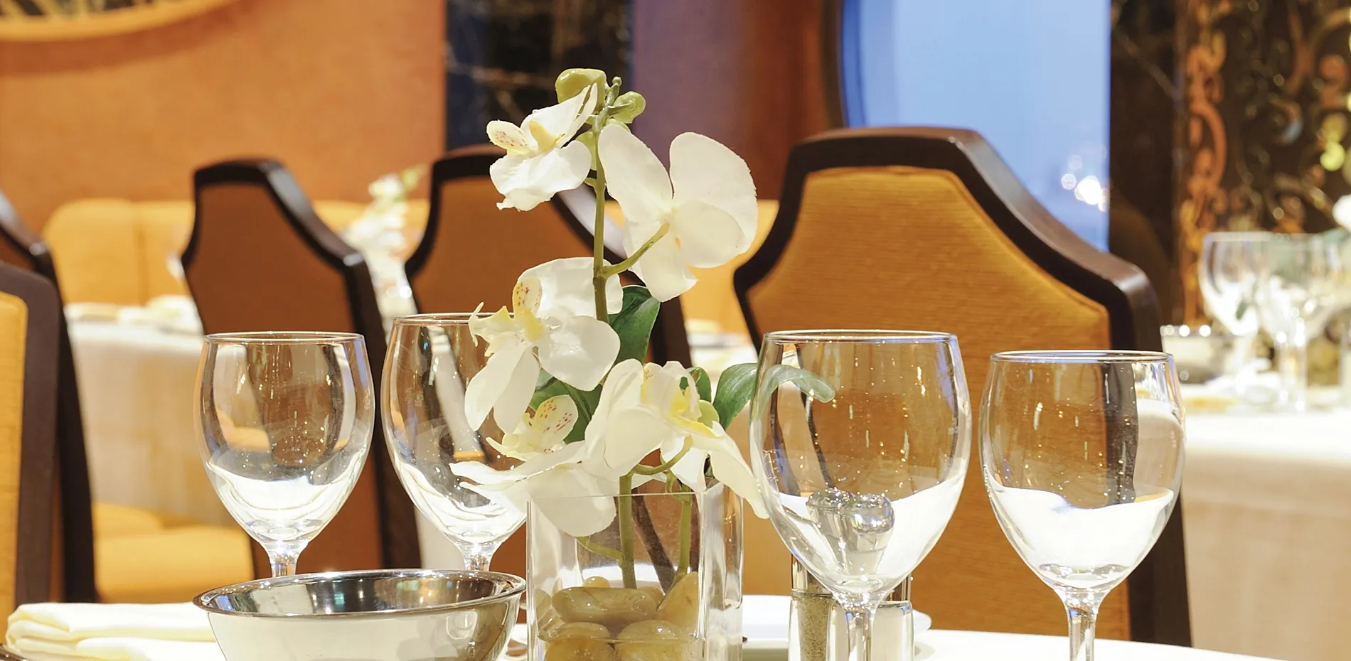 Elegant table setting with white orchid, wine glasses, and yellow chairs