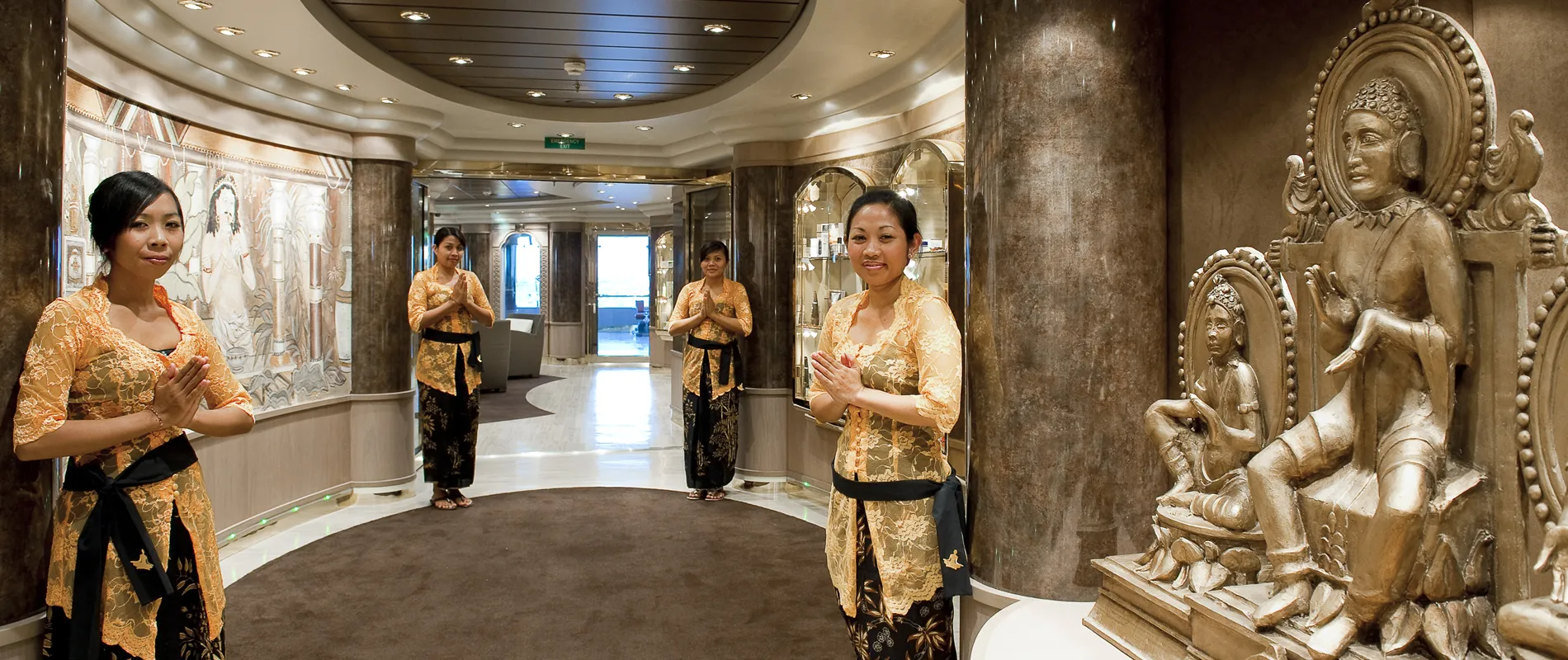 Traditional dressed women greeting in luxurious cruise ship corridor with statues