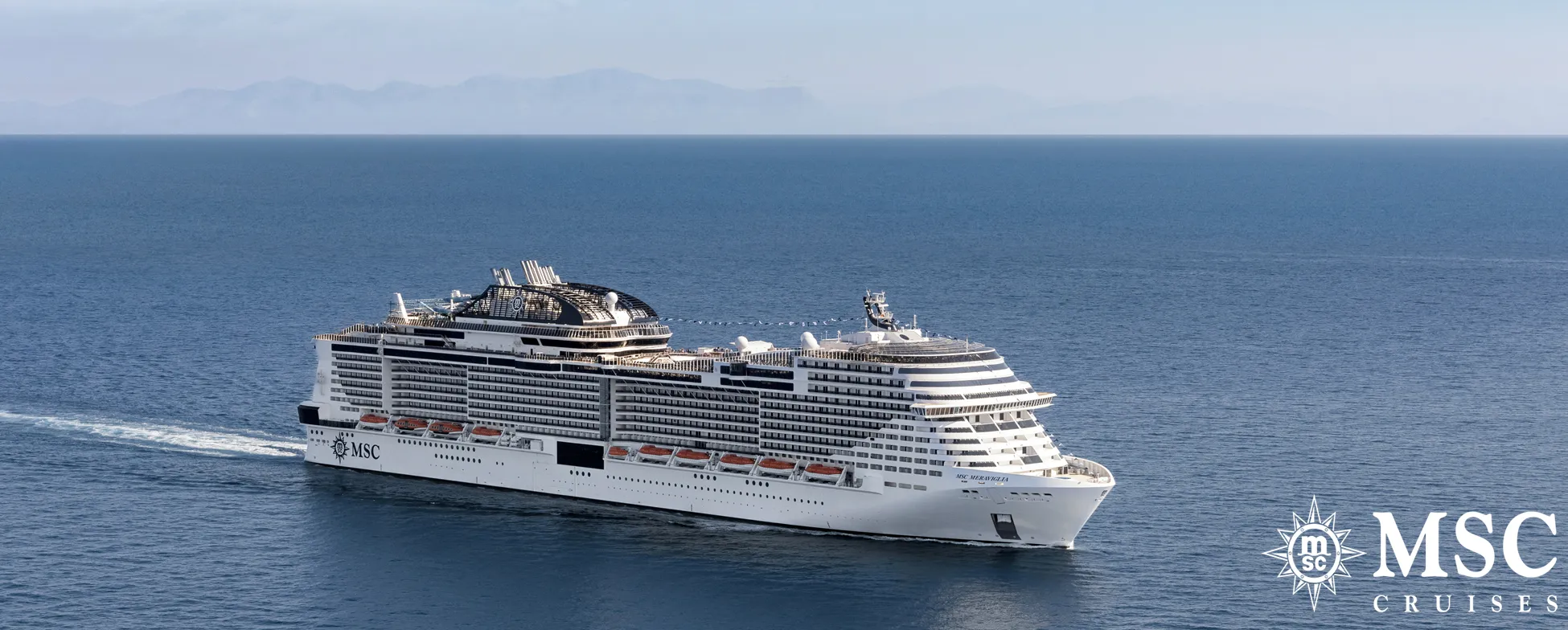 Large white MSC cruise ship sailing on blue ocean with mountains in background