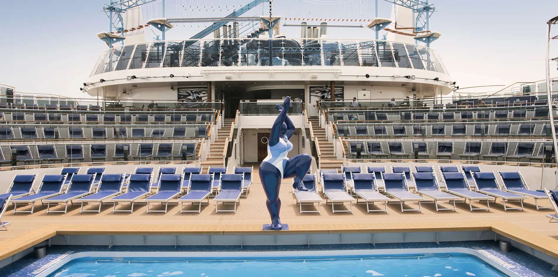 Cruise ship deck with blue statue, lounge chairs, and swimming pool