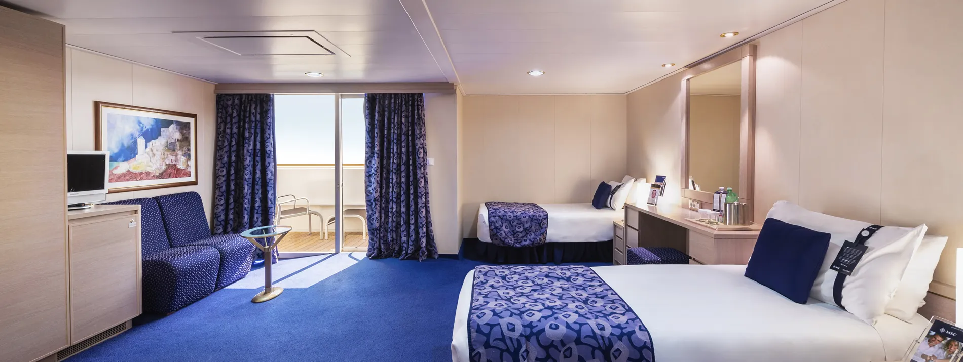 Spacious cruise ship cabin with blue carpet, white bed, and balcony