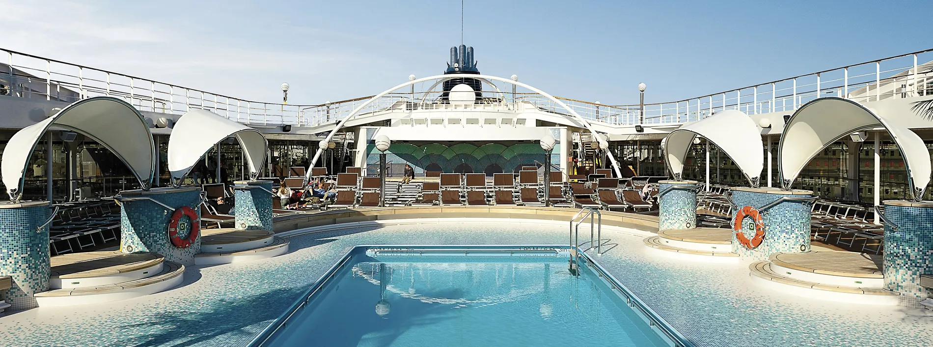 Luxury cruise ship pool deck with blue water and white curved canopies