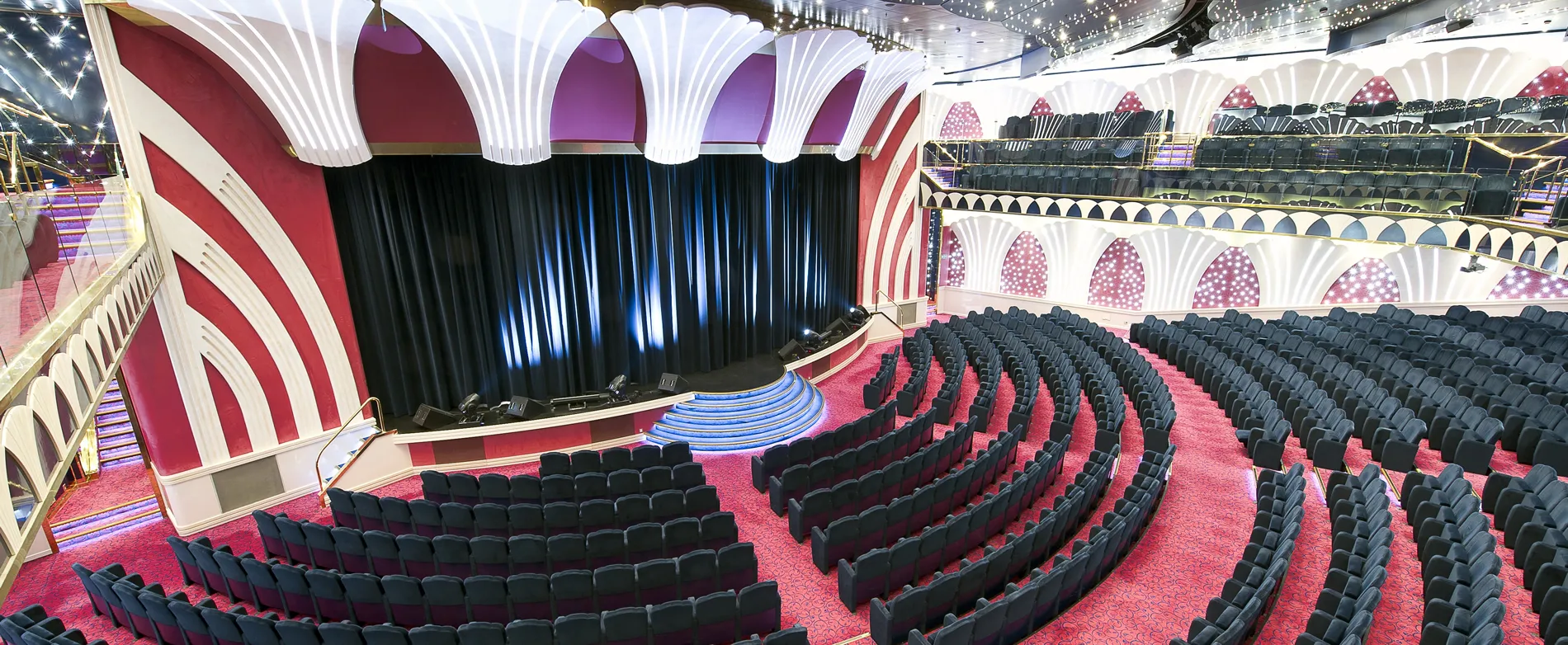 Ornate theater interior with red carpet, curved seating, and dramatic stage