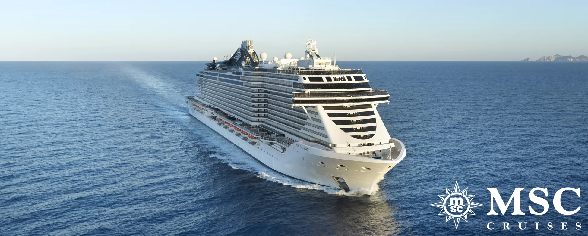 Large white MSC cruise ship sailing on blue ocean with distant land