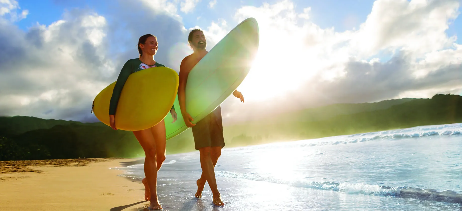 Two surfers with yellow and green boards walking on sunny beach
