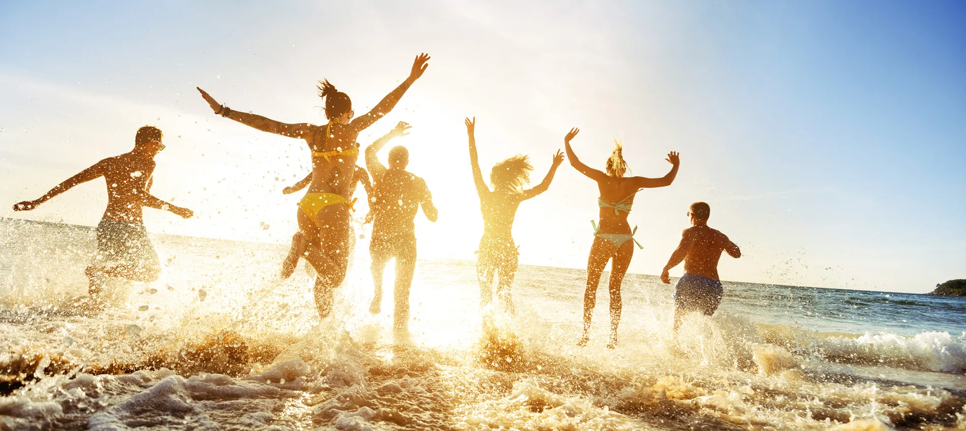 Friends jumping in ocean waves at sunset, creating joyful water splash