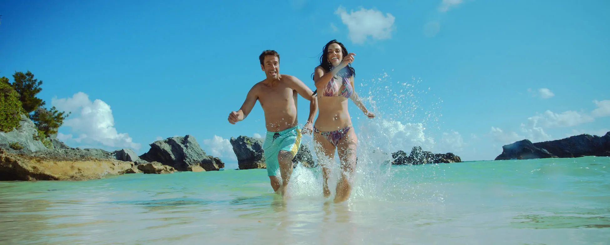 Two people joyfully running and splashing in turquoise beach water