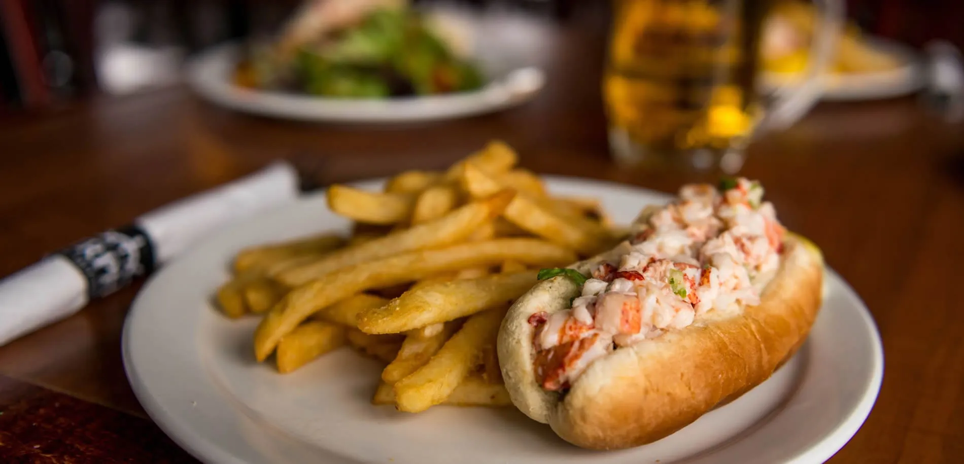 Lobster roll with golden french fries on a white plate