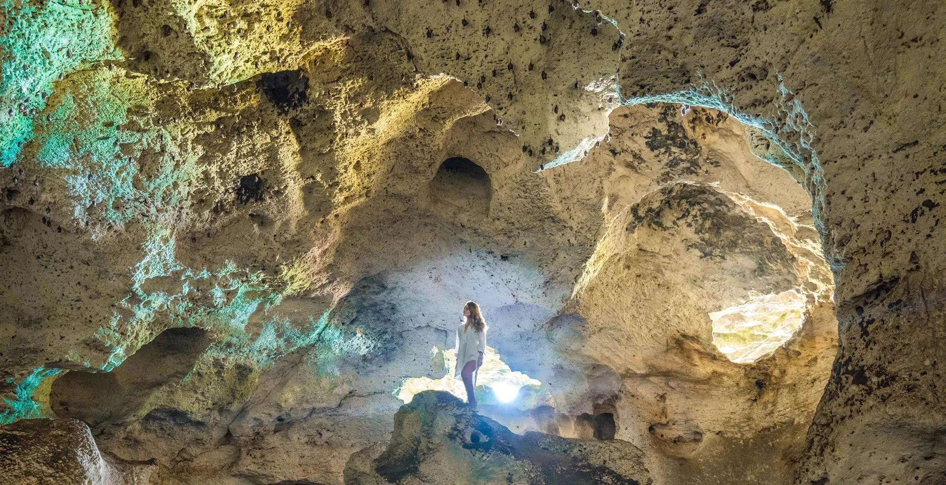 Person standing in illuminated rocky cave with colorful stone walls