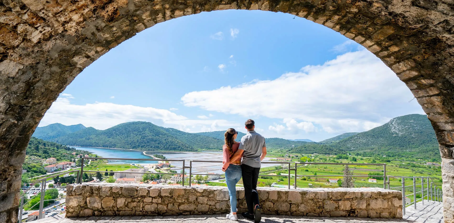 Couple admiring scenic mountain valley and lake through stone archway