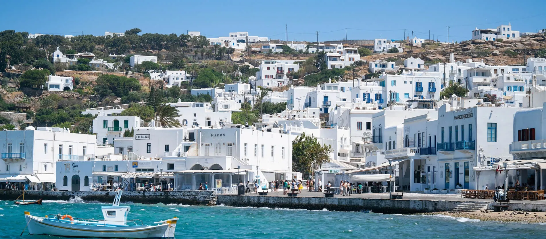 White-washed Greek island town of Mykonos with blue waters and traditional boat
