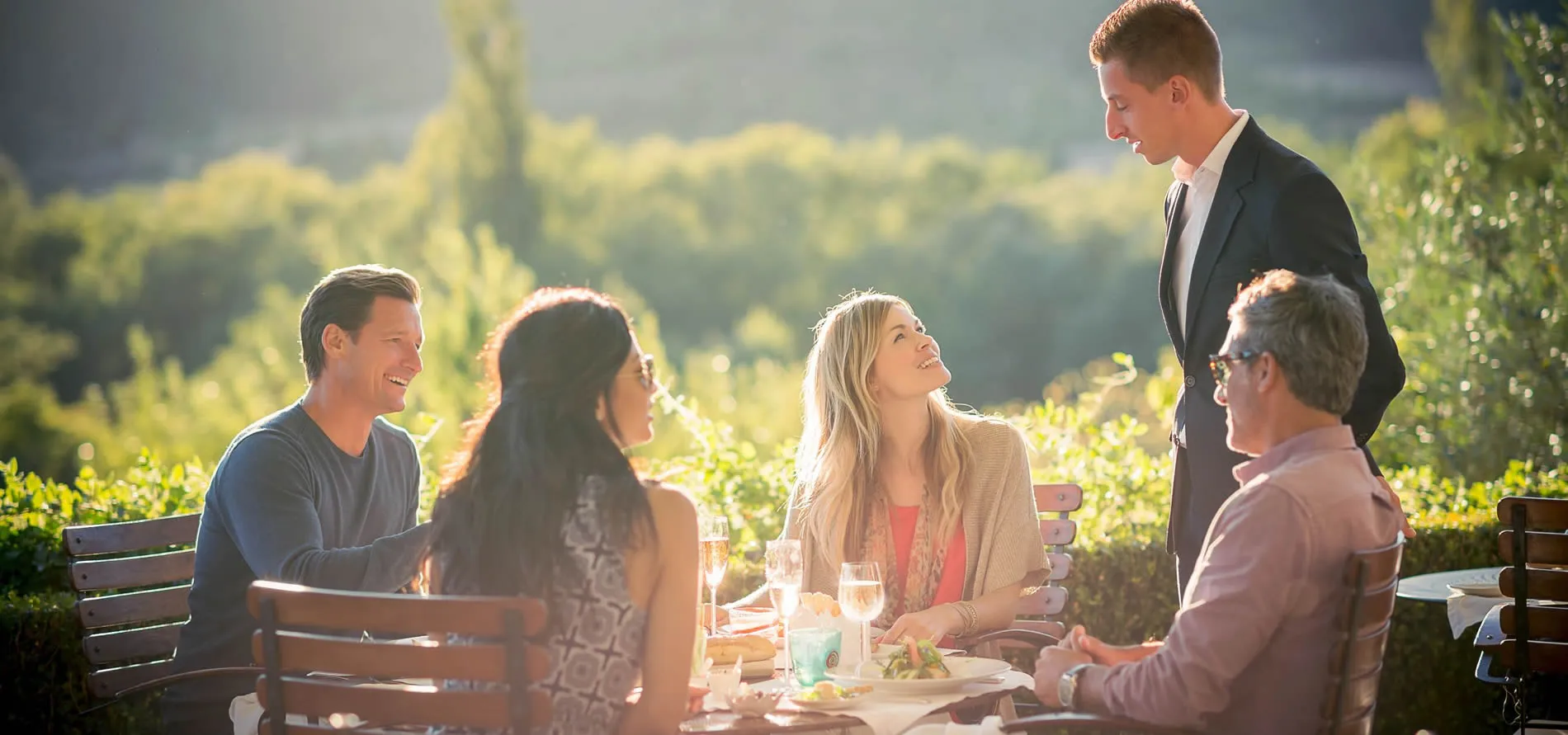 Friends enjoying outdoor lunch at sunny vineyard with wine and conversation