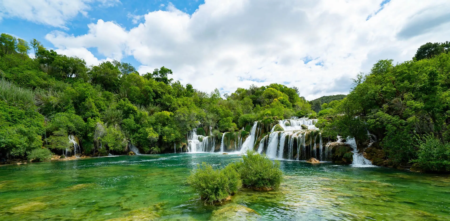 Lush green waterfalls cascading into turquoise pools surrounded by forest